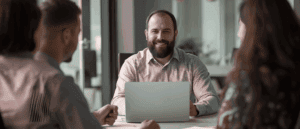 Showing the attributes of a inspirational leader - man sitting at a meeting with his team and computer.