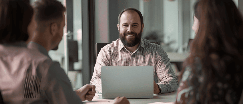 Showing the attributes of a inspirational leader - man sitting at a meeting with his team and computer.