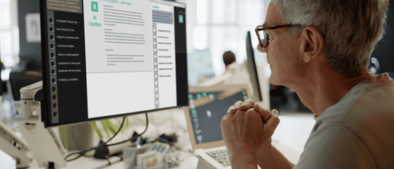 An older man attentively observes an AI chatbot on his screen, reflecting on the intersection of leadership development and artificial intelligence.